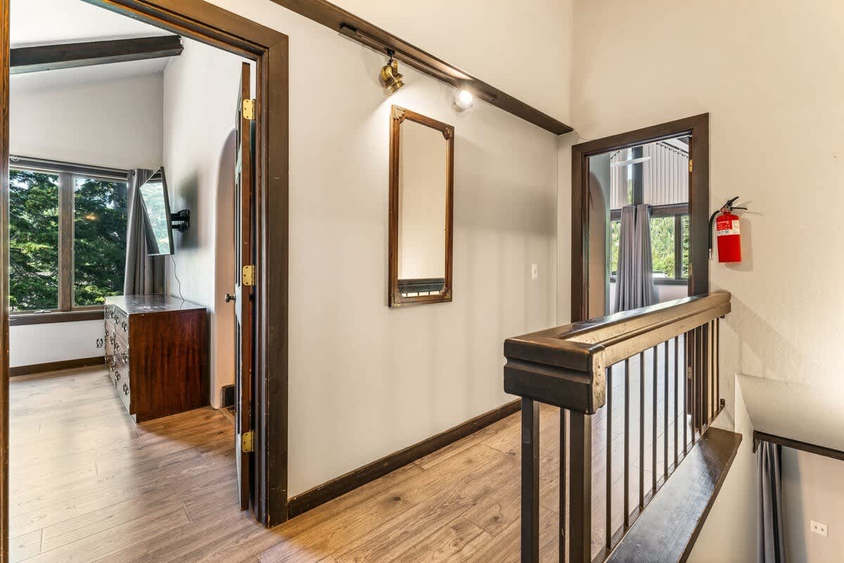 Hallway in an Olympic Valley vacation rental with wooden floors and a wall mirror, leading to rooms with large windows.