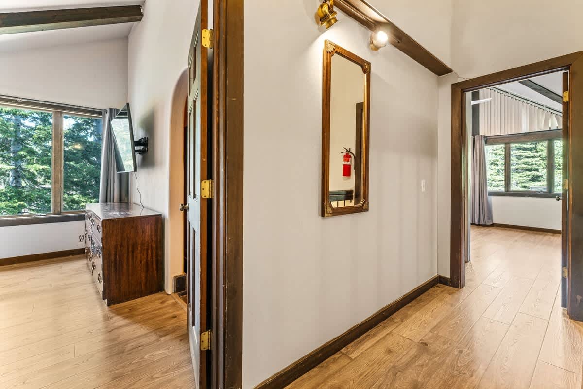 Hallway with wooden flooring in Olympic Valley vacation rental; features a mirror and view into adjacent rooms with large windows.