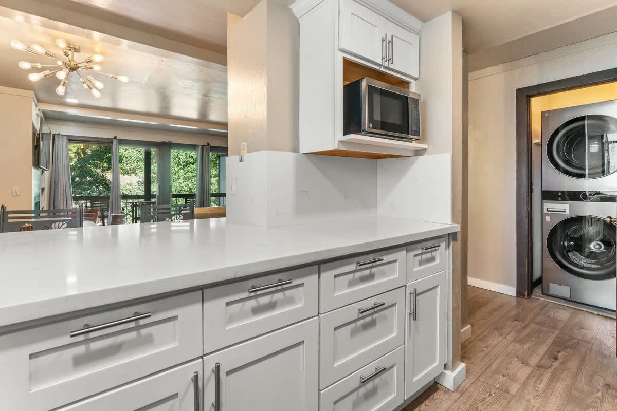 Modern kitchen in Olympic Valley vacation rental, featuring white cabinets, microwave, and a view of lush greenery.