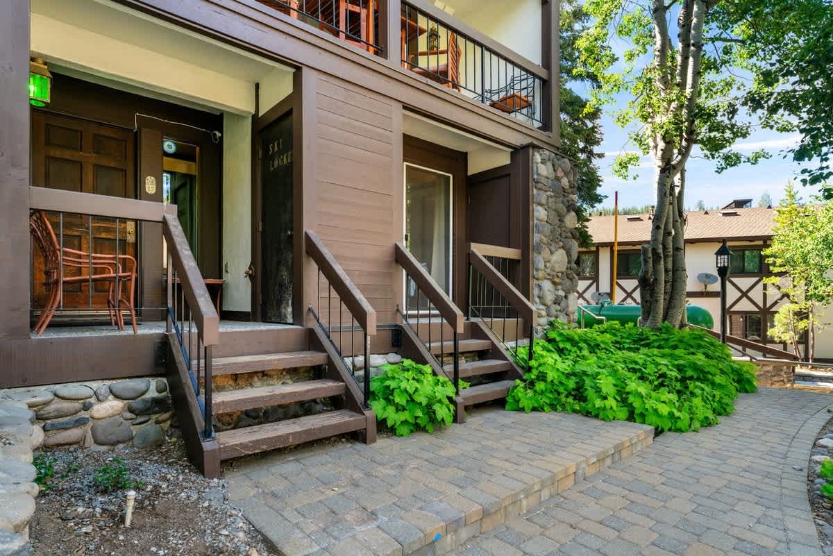 Brown wooden vacation rental in Olympic Valley with stone accents, two staircases, and lush greenery.