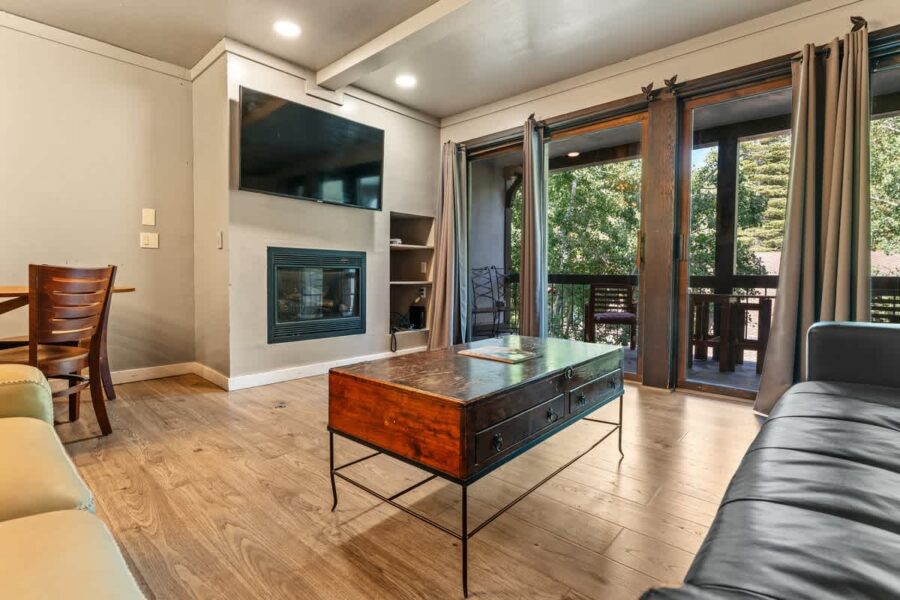 Cozy living room in an Olympic Valley vacation rental with a fireplace, TV, and balcony view.