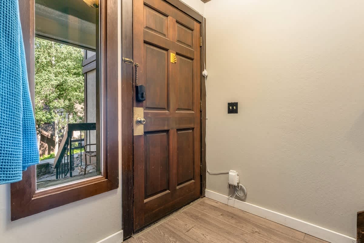 Entrance of an Olympic Valley vacation rental with wooden door and window view of trees and outdoor stairs.