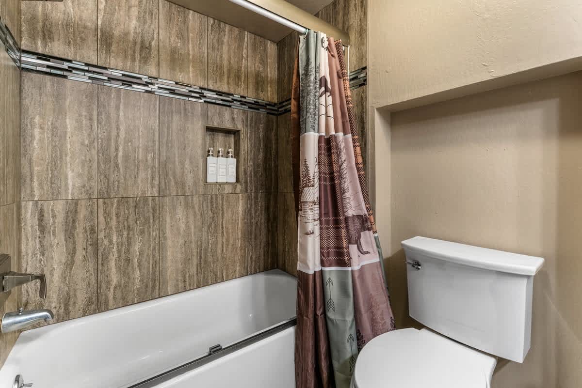 Bathroom with a tub, shower curtain, and toilet in an Olympic Valley vacation rental.