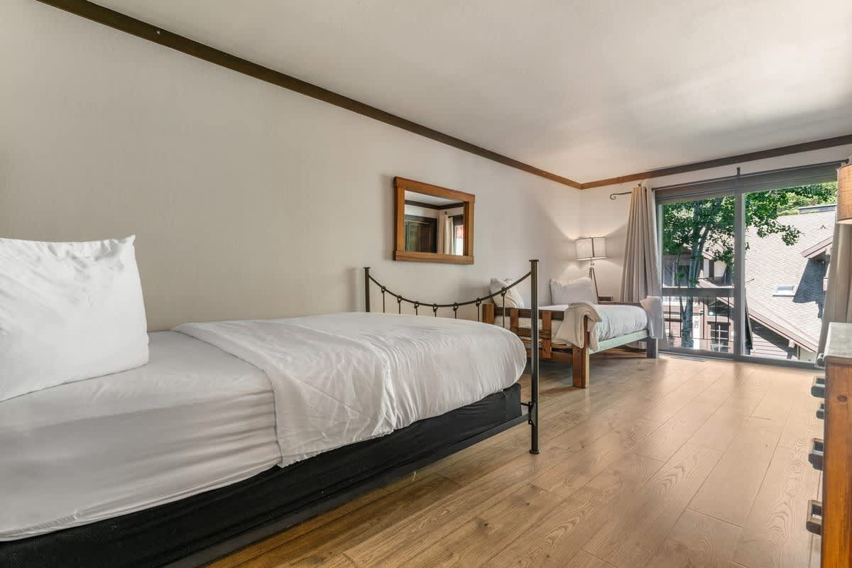 Bright double bedroom in Olympic Valley vacation rental with balcony view, hardwood floor, and cozy beds.