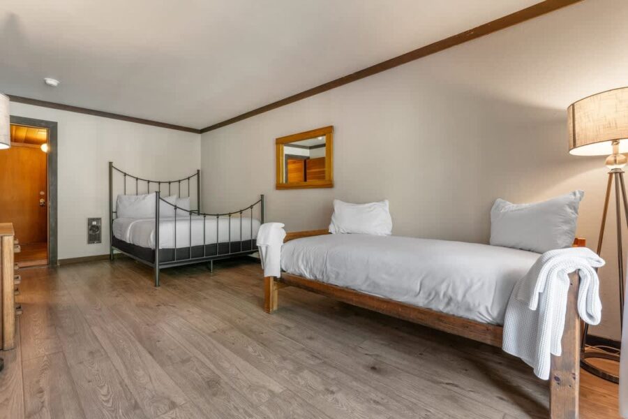 Two cozy beds in an Olympic Valley vacation rental room with wooden flooring and modern decor.