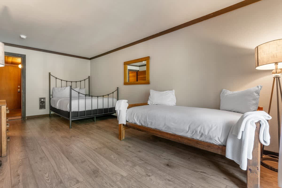 Two cozy beds in an Olympic Valley vacation rental room with wooden flooring and modern decor.