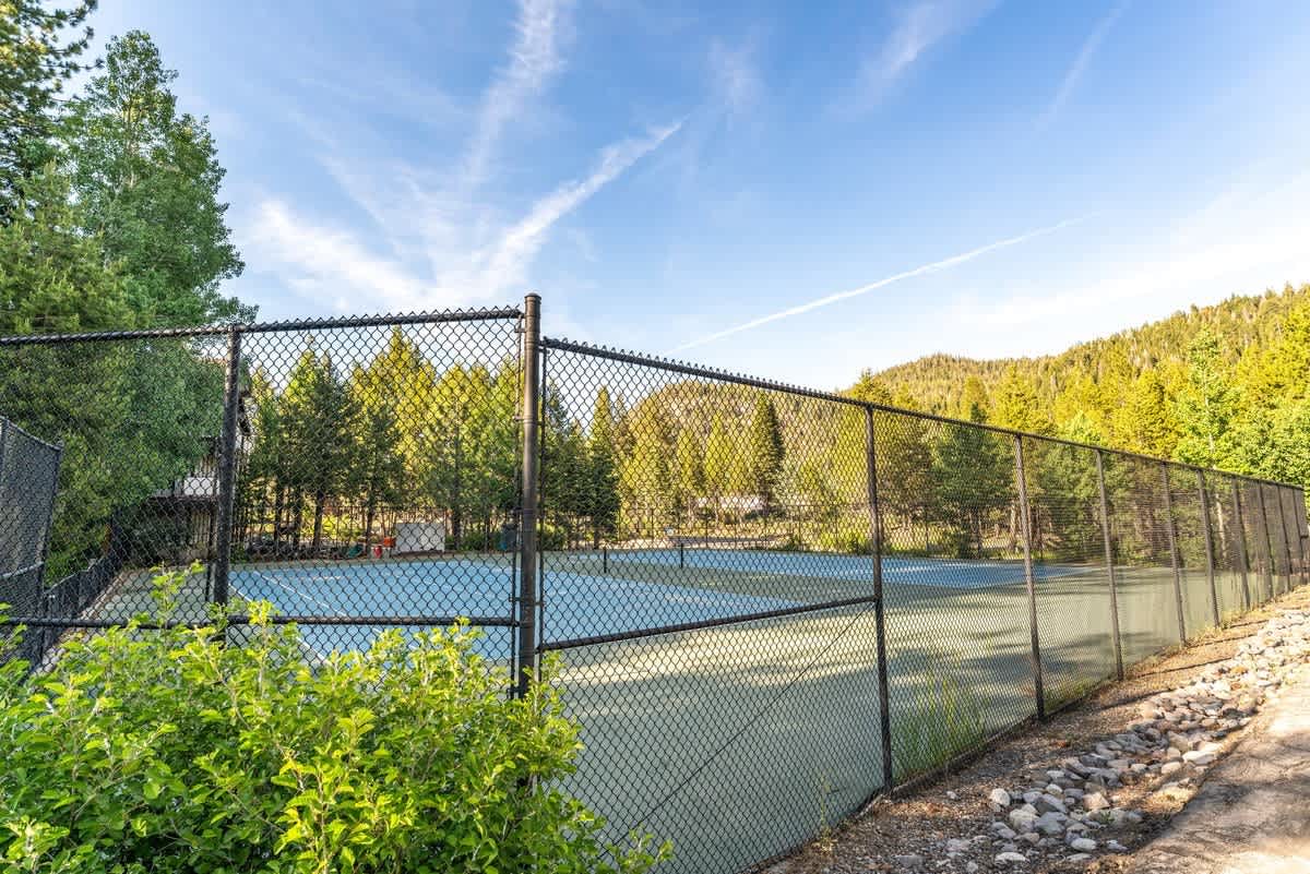 Tennis court near vacation rental in Olympic Valley, surrounded by lush trees and mountains under a clear blue sky.