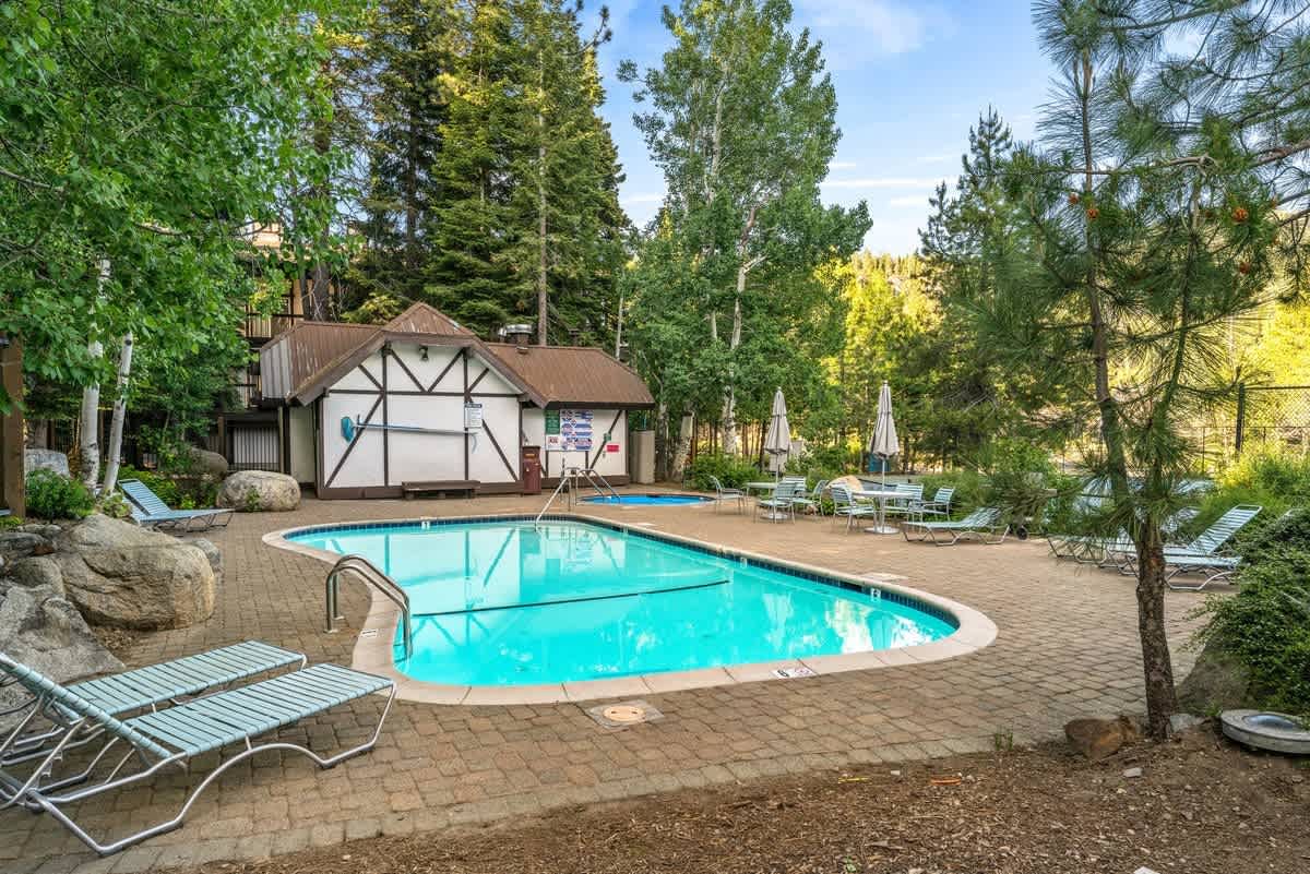 Poolside area at a vacation rental in Olympic Valley, surrounded by trees and lounge chairs for relaxation.