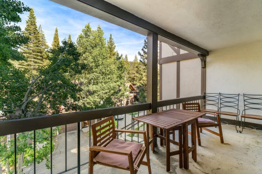 Balcony view from an Olympic Valley vacation rental, with wooden furniture and lush trees in the background.