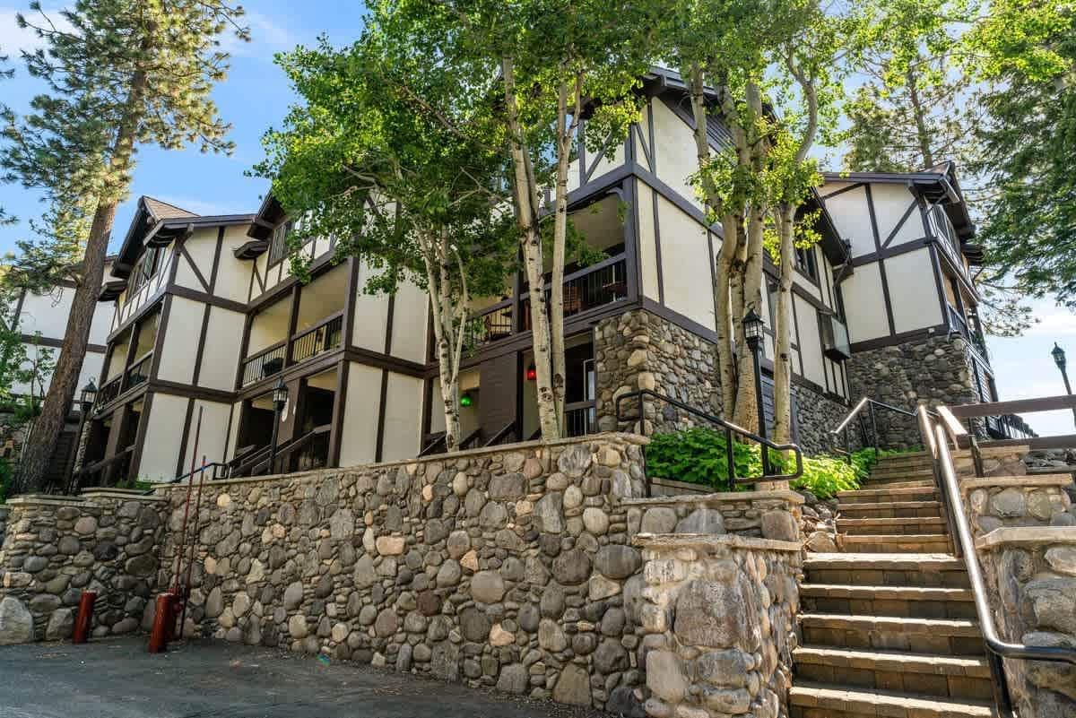 Tudor-style vacation rental with stone facade and lush trees in Olympic Valley. Steps leading to entrance.