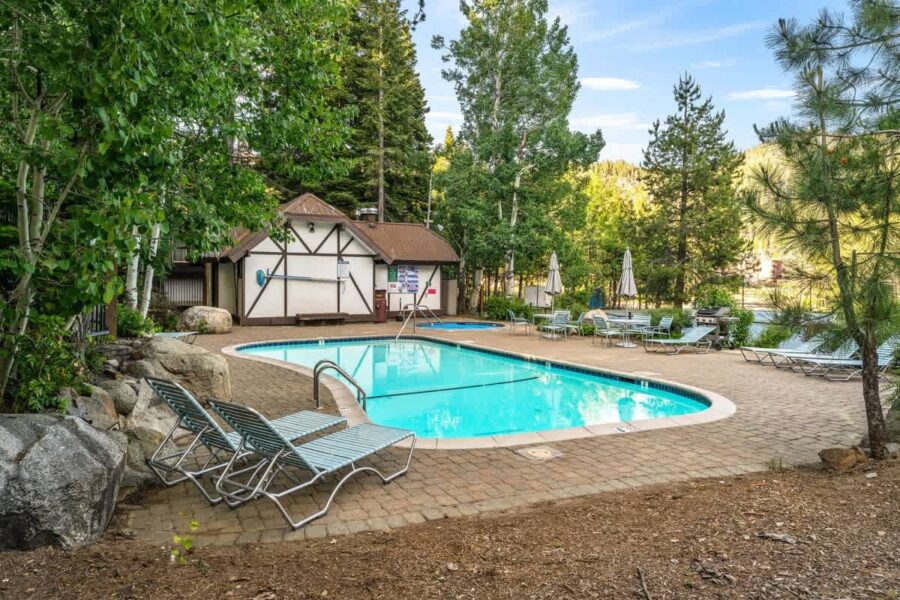 Outdoor pool at a vacation rental in Olympic Valley, surrounded by trees and lounge chairs on a sunny day.