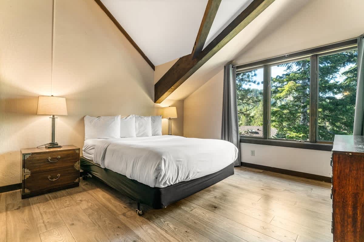 Bedroom with large window and wooden beams in an Olympic Valley vacation rental, featuring a bed, lamps, and nightstands.