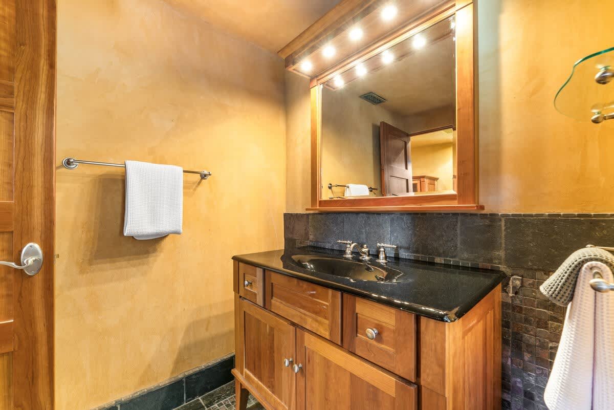 Modern bathroom in Olympic Valley vacation rental with wooden vanity, black countertop, and large mirror.