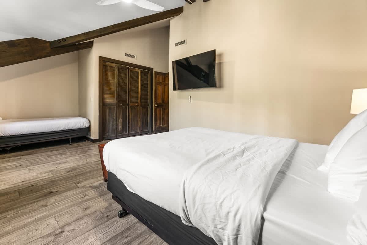 Cozy bedroom with two beds and a TV in an Olympic Valley vacation rental, featuring wooden beams and floor.