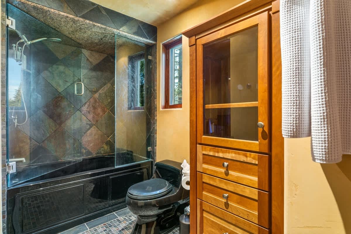 Modern bathroom in Olympic Valley vacation rental with tiled shower, wood cabinet, and window.