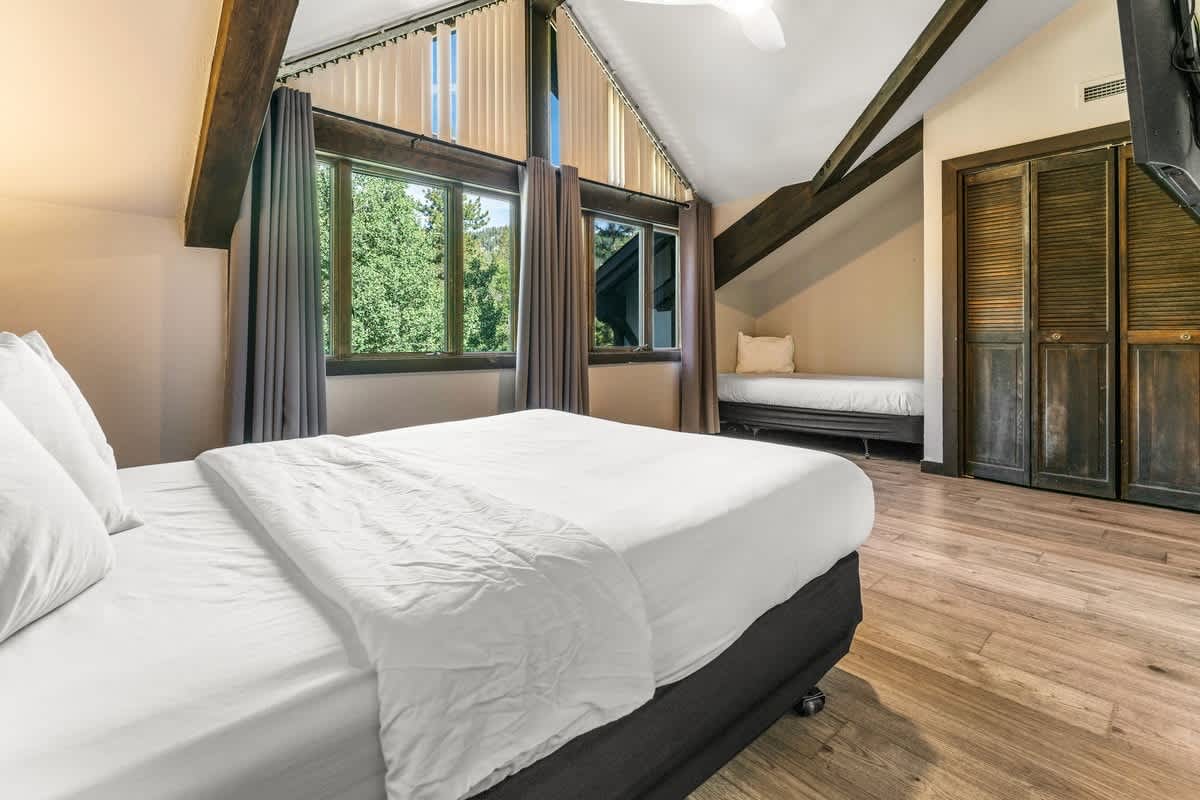 Cozy bedroom in a vacation rental, featuring wooden beams and large windows with forest views in Olympic Valley.