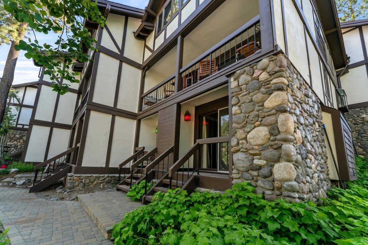 Tudor-style vacation rental with stone accents in Olympic Valley, surrounded by lush greenery and a paved pathway.