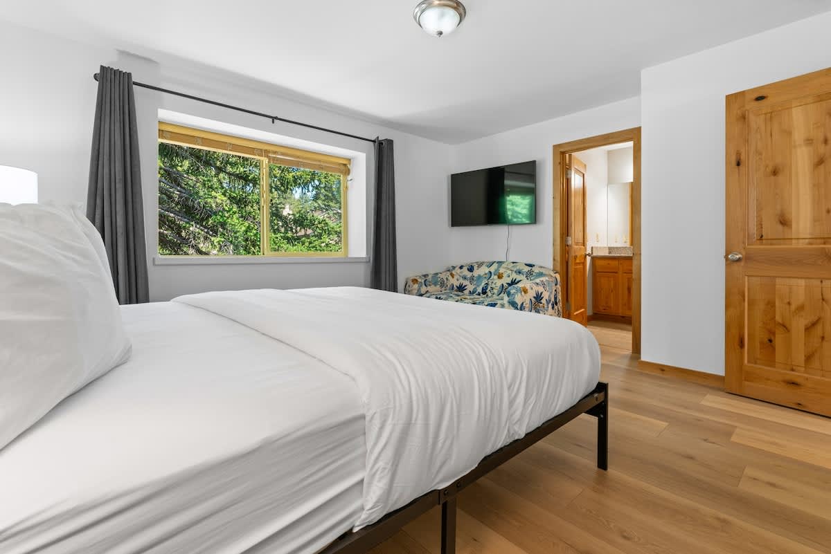 Bright bedroom in a Tahoe City vacation rental with large window, white bedding, floral couch, and wall-mounted TV.