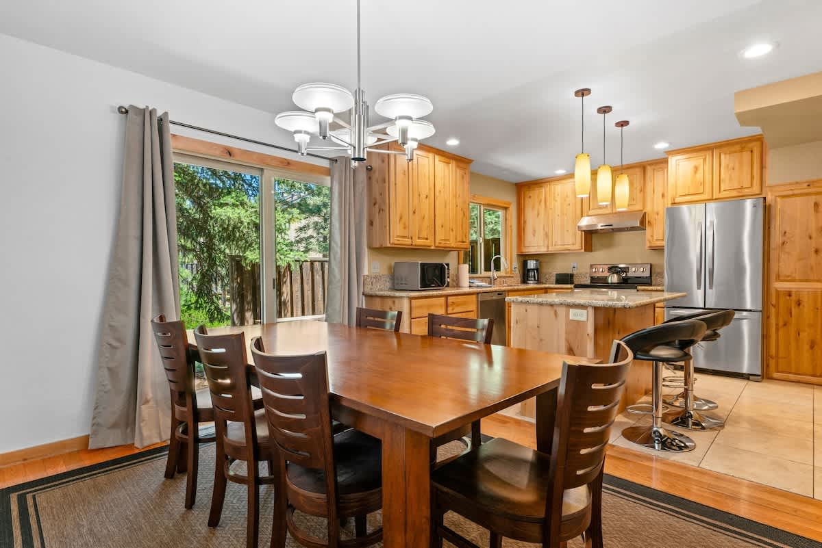 Dining area and kitchen in a Tahoe City vacation rental with wooden cabinets, table, and modern appliances.