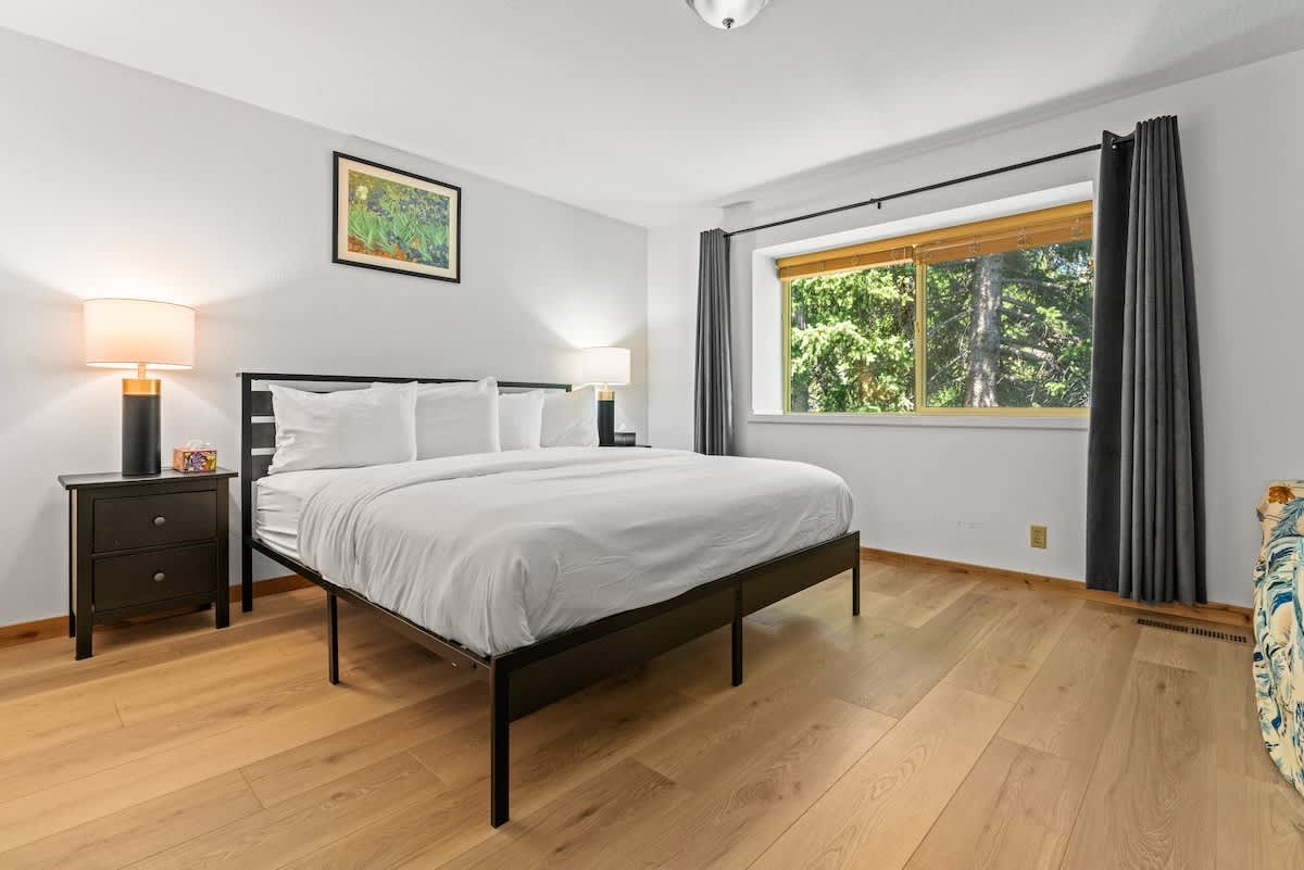 Modern bedroom in a Tahoe City vacation rental with a large bed, wooden floors, and a bright window view.