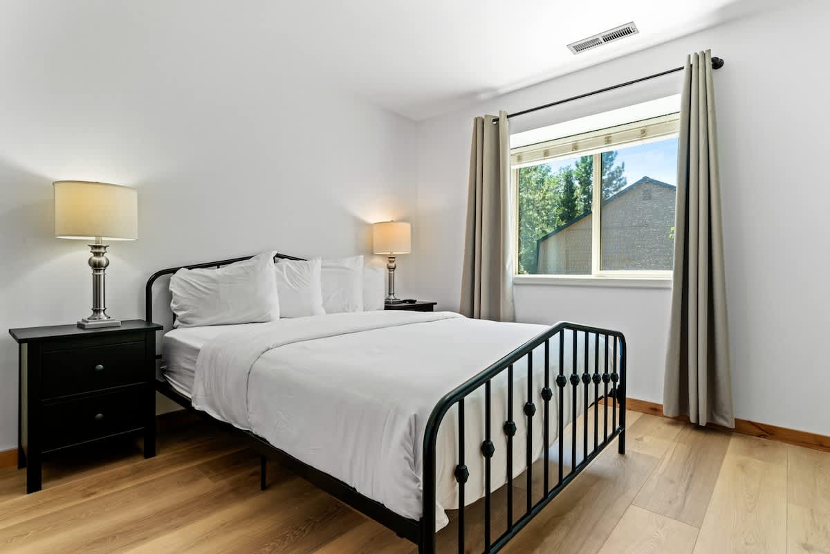 Bedroom in Tahoe City vacation rental with a cozy bed, bedside tables, and a window view of trees.