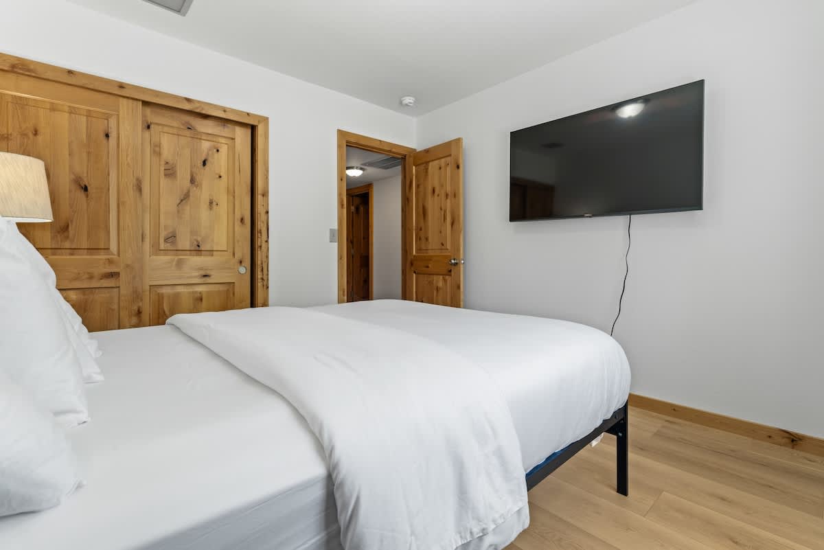 Bedroom in a Tahoe City vacation rental with white bedding, wooden doors, and a wall-mounted TV.