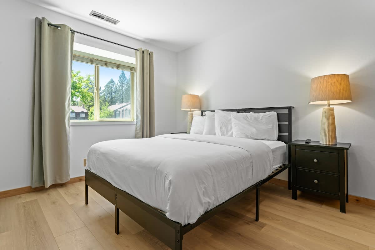 Bright bedroom in a Tahoe City vacation rental, featuring a cozy bed, lamps, and a window with a scenic view.