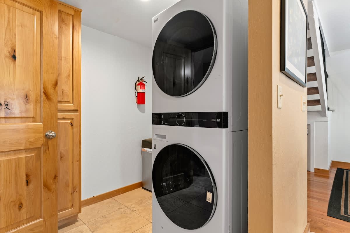 Stacked washer and dryer in a Tahoe City vacation rental laundry area with wooden cabinets and stairs nearby.