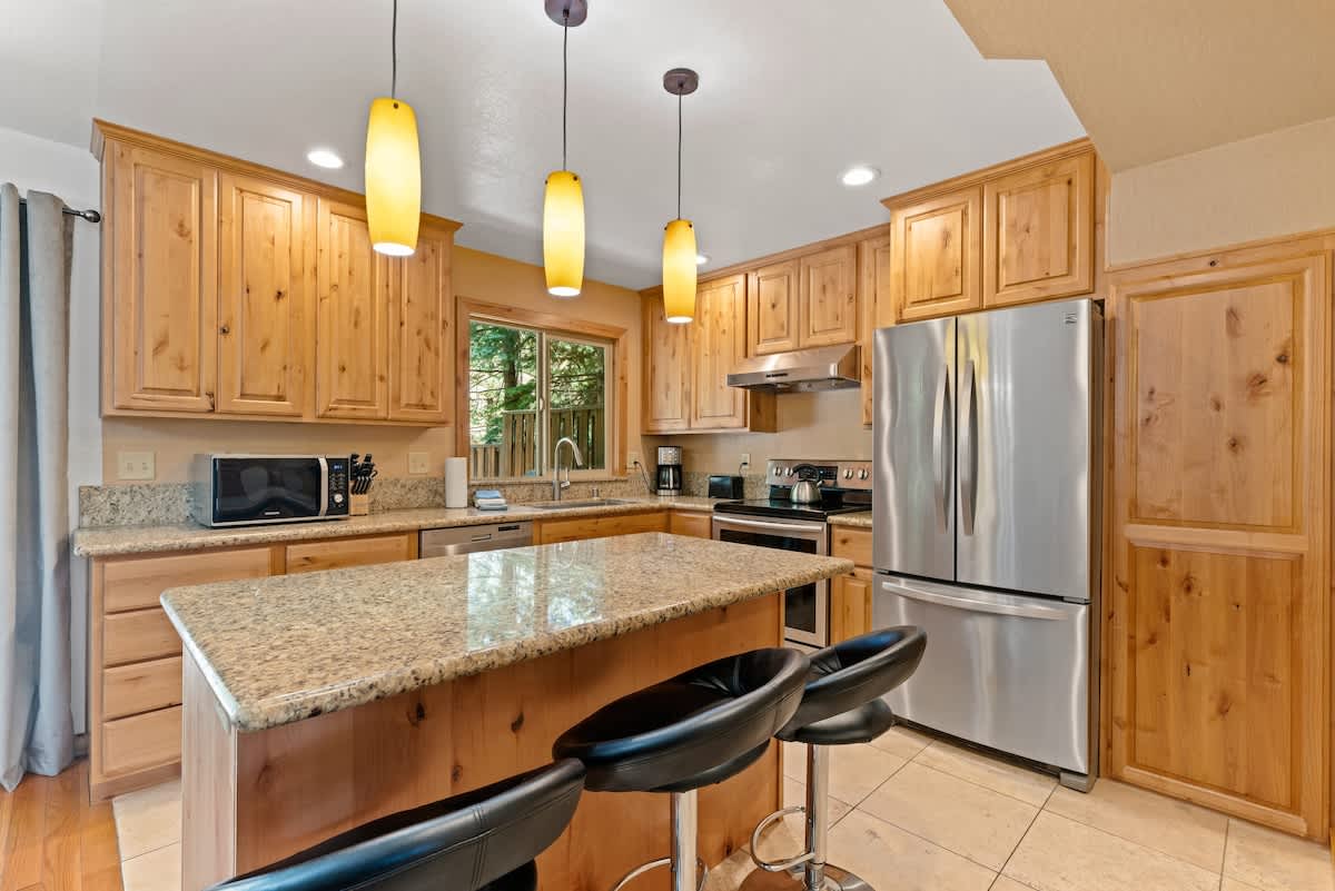 Modern kitchen in Tahoe City vacation rental with wooden cabinets, granite island, stainless appliances, and pendant lights.