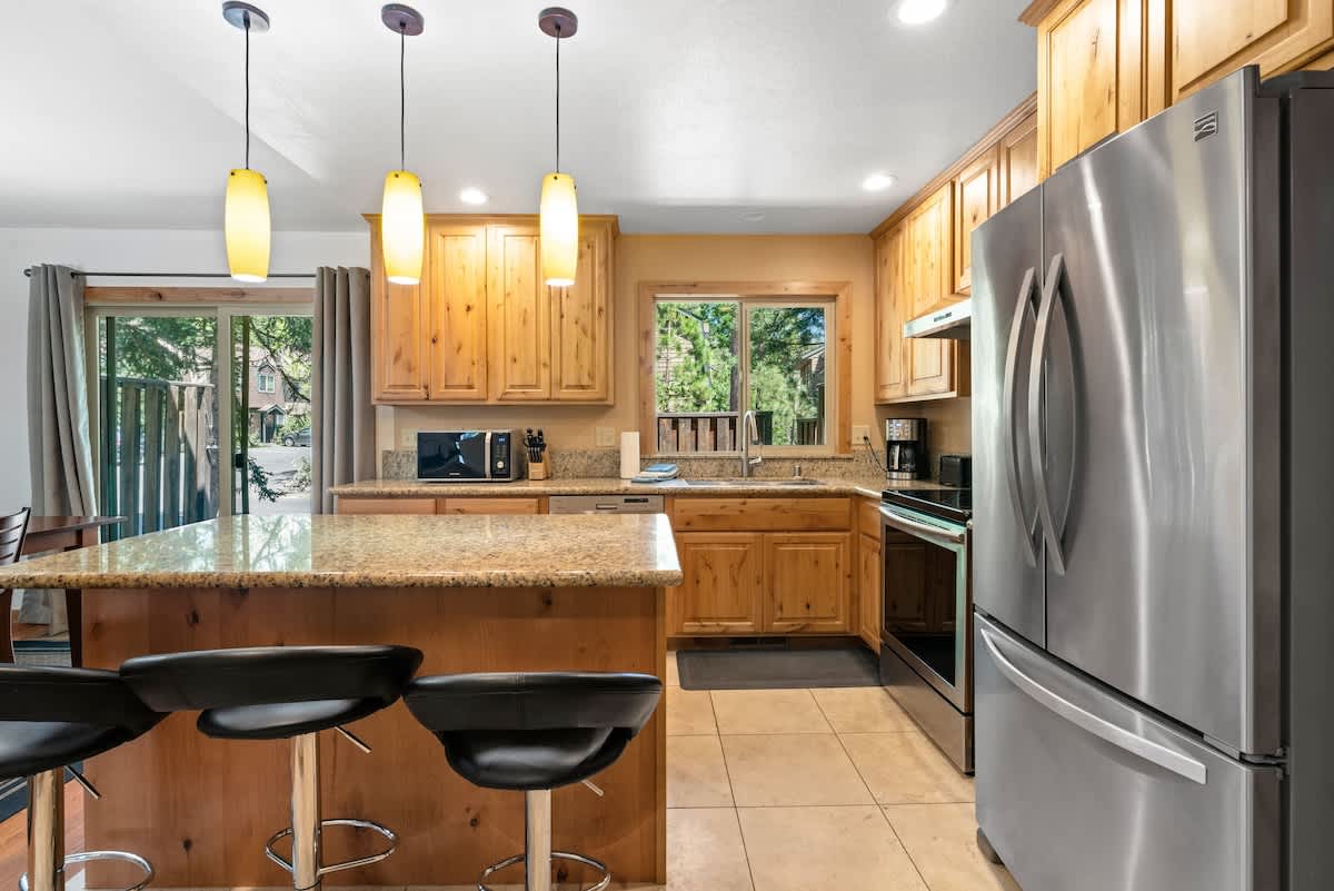 Modern kitchen in a Tahoe City vacation rental with granite countertops, stainless steel appliances, and wooden cabinets.