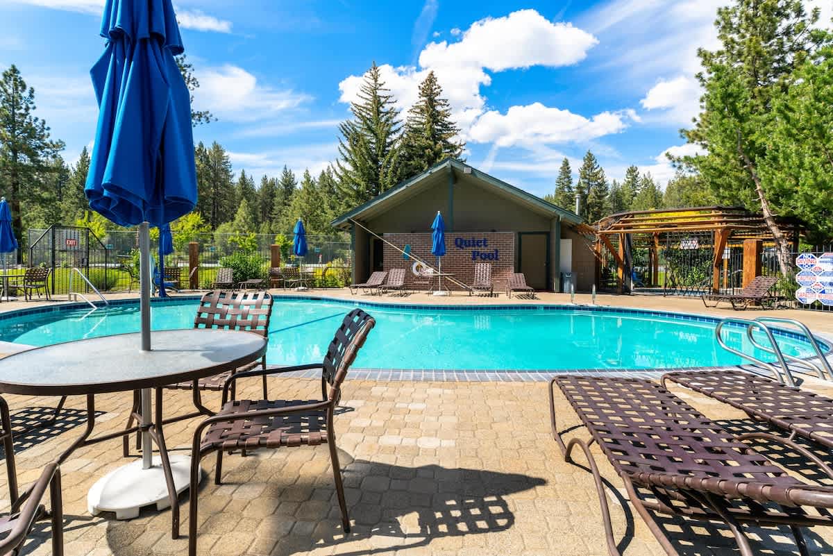 Poolside view of Tahoe City vacation rental with lounge chairs, umbrellas, surrounded by trees and blue sky.