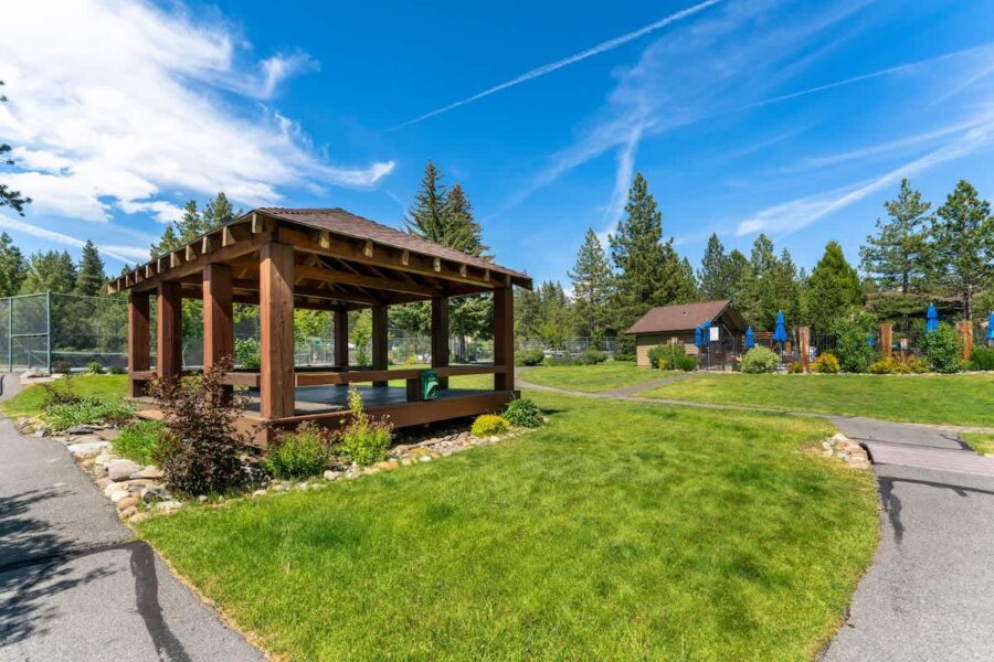 A spacious lawn with a wooden pavilion near a vacation rental in Tahoe City, surrounded by trees under a clear blue sky.