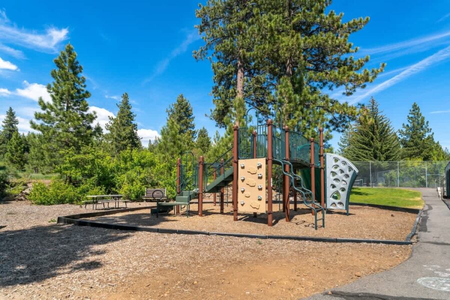 Playground area near Tahoe City vacation rental with climbing structures, surrounded by tall pine trees and blue sky.