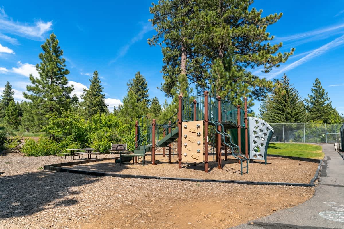 Playground area near Tahoe City vacation rental with climbing structures, surrounded by tall pine trees and blue sky.