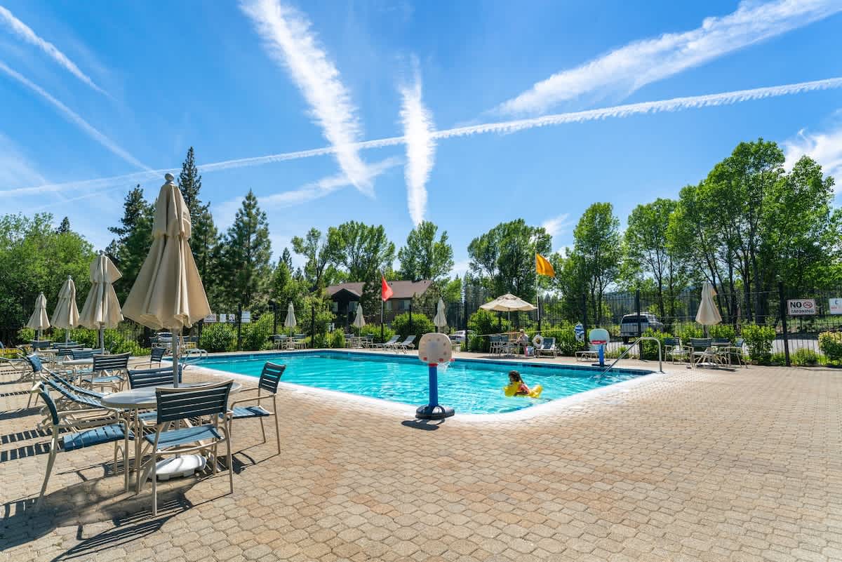 Poolside view at a Tahoe City vacation rental with lounge chairs, umbrellas, and clear skies in the background.