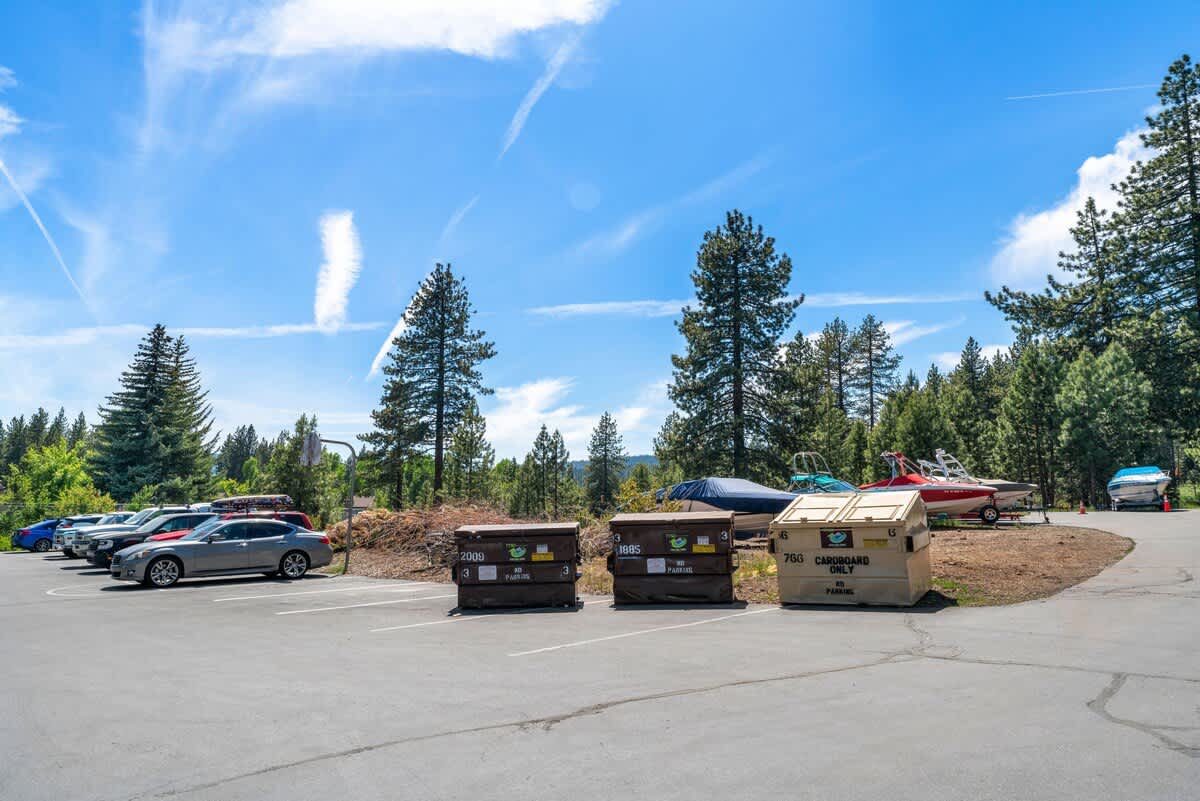 Parking area with boats and dumpsters near a Tahoe City vacation rental, surrounded by pine trees under a blue sky.