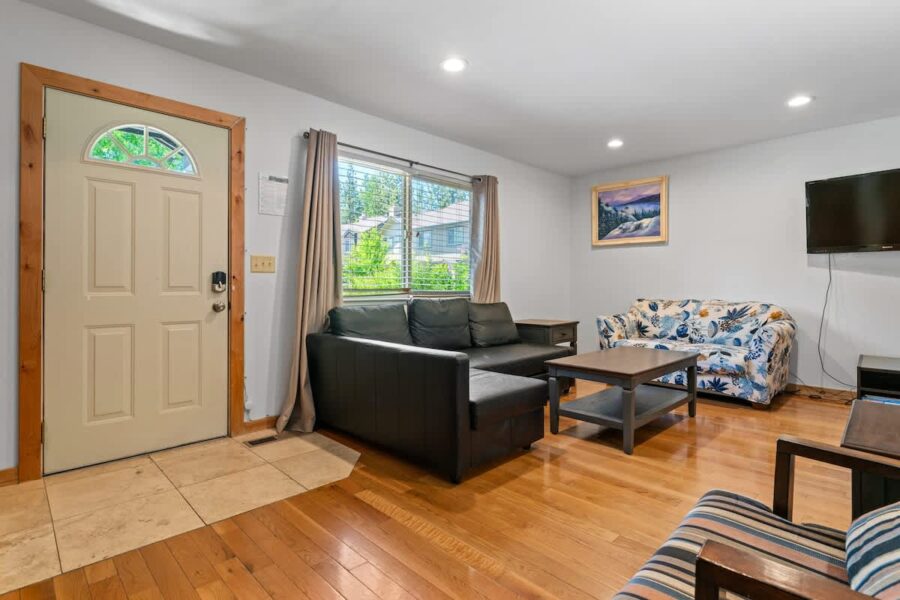 Cozy living room in Tahoe City vacation rental with sofas, TV, and window view. Warm wooden flooring and decor.