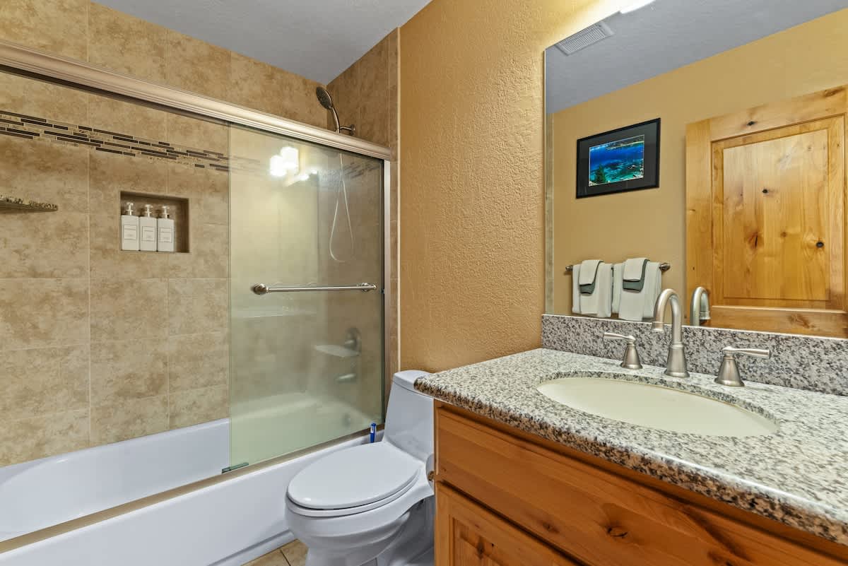 Bathroom in Tahoe City vacation rental with granite sink, wooden cabinetry, and a glass-enclosed shower.