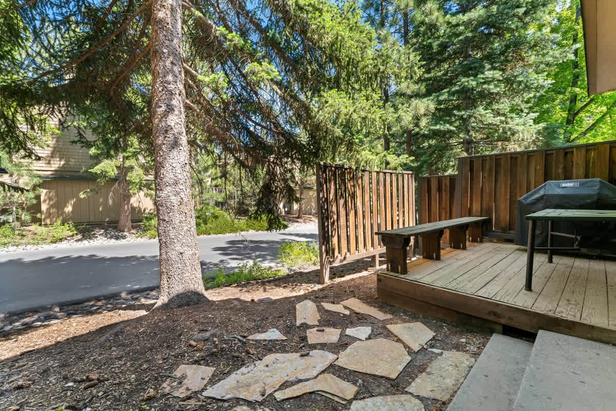 Cozy Tahoe City vacation rental with a wooden deck, bench, and grill, surrounded by lush trees and nature.