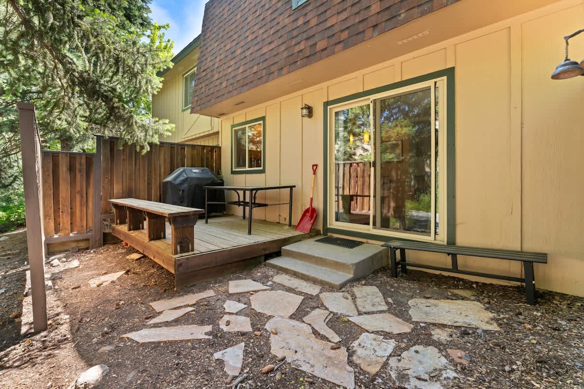 Backyard view of a Tahoe City vacation rental with a small wooden deck, table, barbecue grill, and stone path.