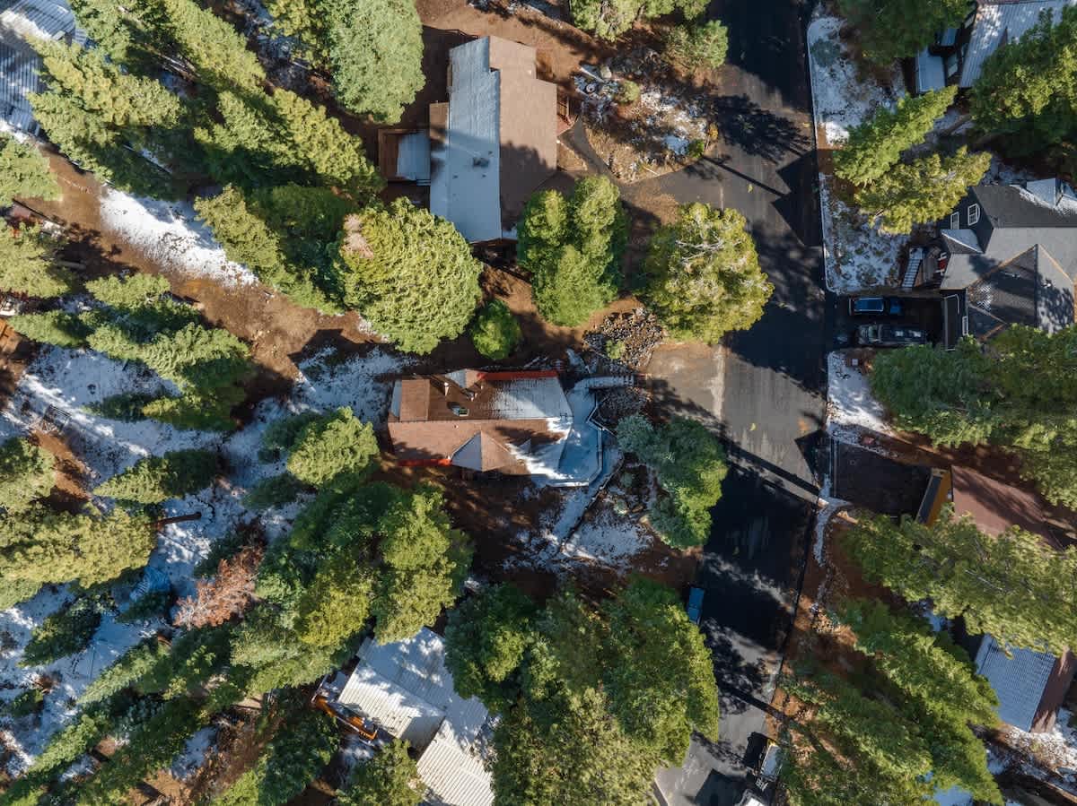 Aerial view of Tahoe Vista vacation rental surrounded by tall pine trees and light snow on roofs and ground.