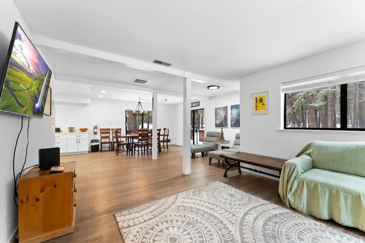 Spacious living room in Truckee vacation rental, featuring modern decor, dining area, and forest views through large windows.