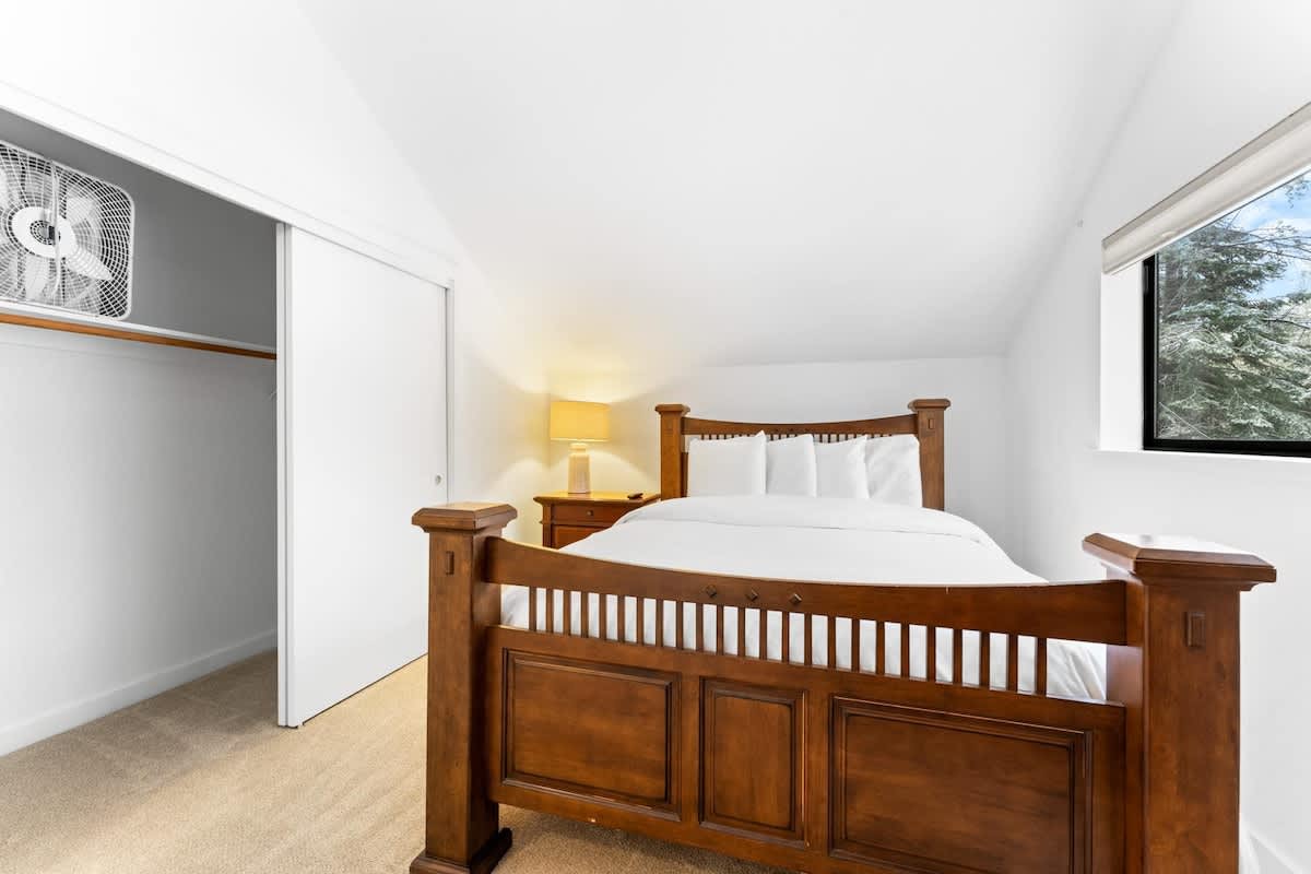 Cozy bedroom in a Truckee vacation rental with a wooden bed, white linens, and a window view of trees.