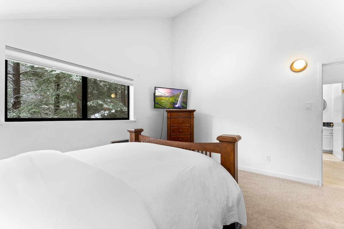 Bedroom in Truckee vacation rental with wooden bed, TV, dresser, and forest view through a large window.