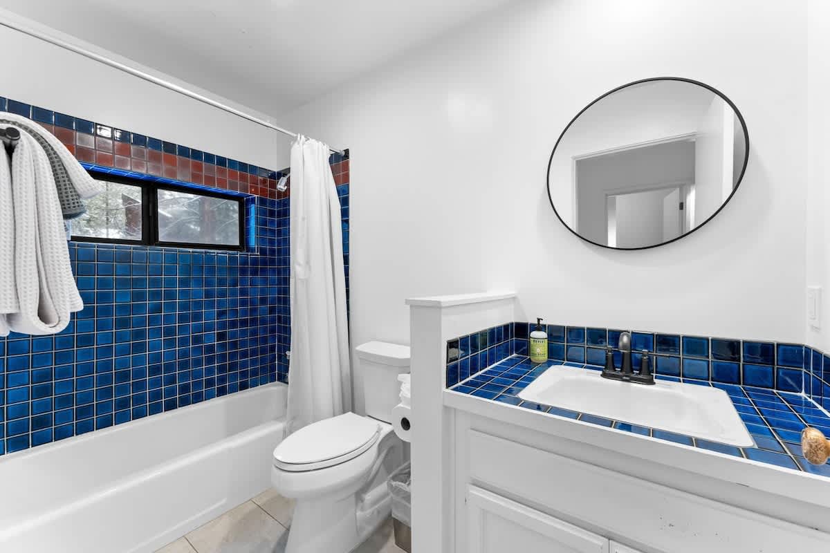 Bathroom in Truckee vacation rental with blue tiled walls, circular mirror, and a white bathtub with curtain.