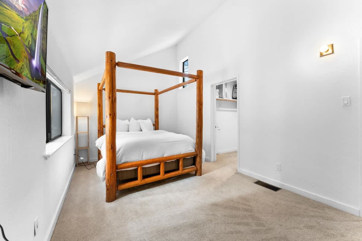 Bright bedroom in a Truckee vacation rental with a wooden canopy bed, white bedding, and a TV on the wall.