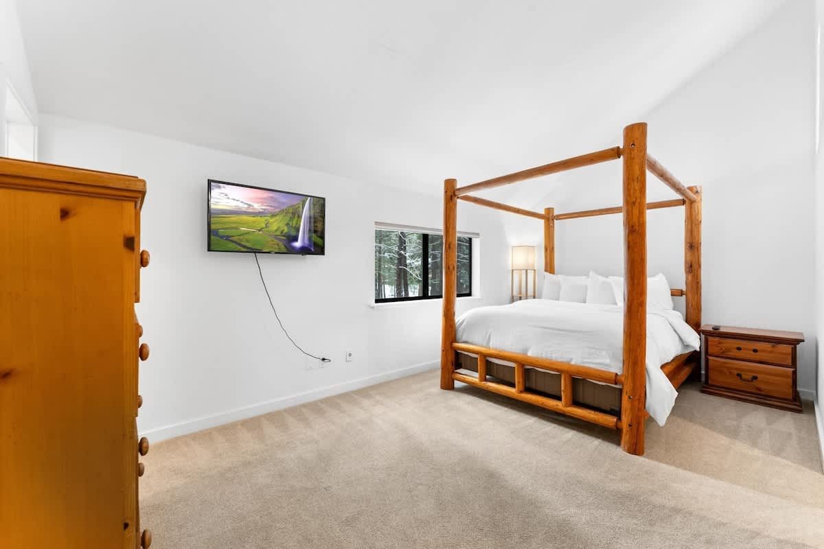 Cozy bedroom in Truckee vacation rental with a wooden bed frame, dresser, TV, and forest views through the window.