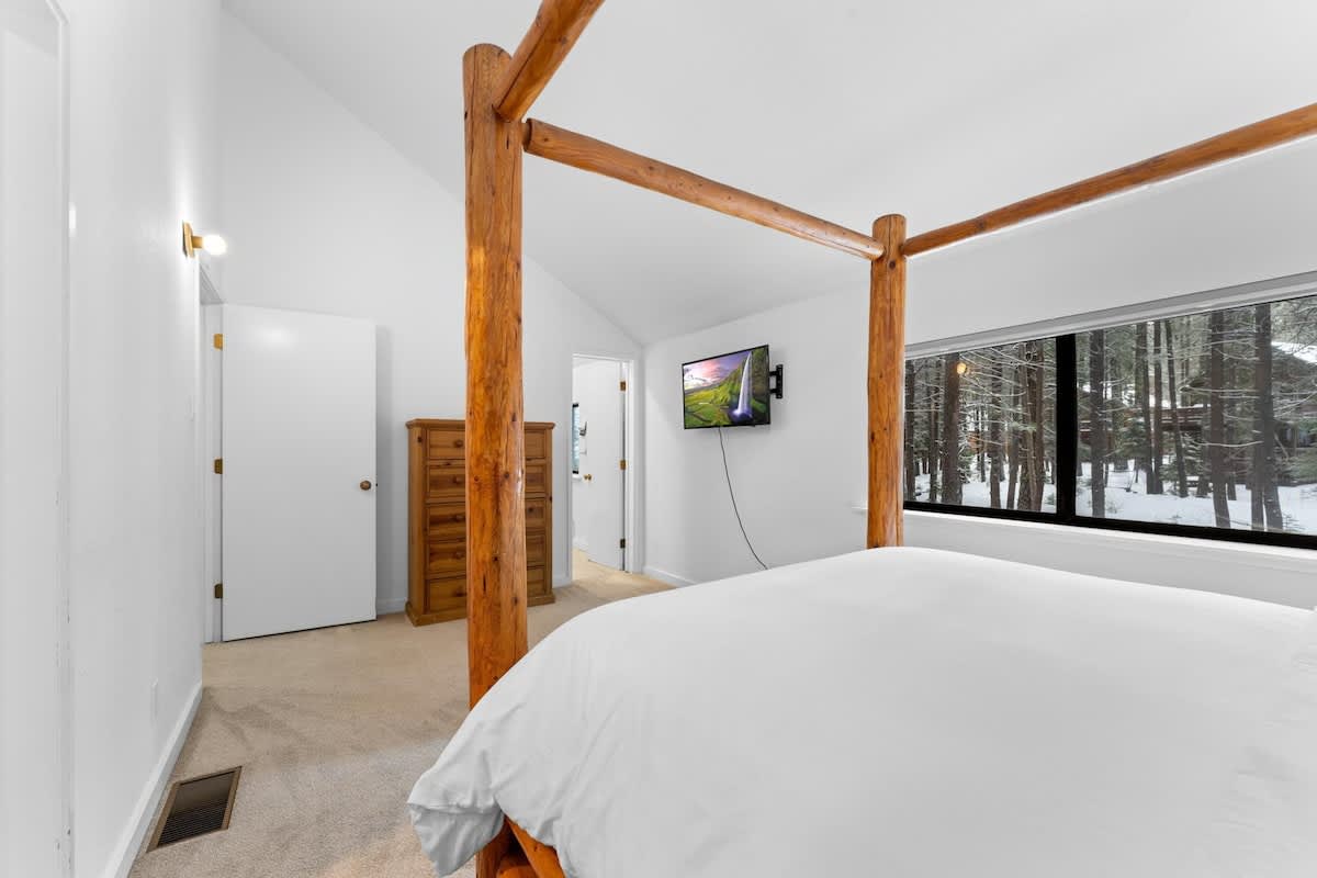 Bedroom in a Truckee vacation rental with a wooden bed frame, TV, and large window showing a snowy forest view.