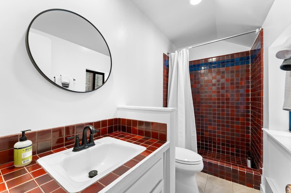 Modern bathroom in a Truckee vacation rental featuring red tiled shower and sink, with a round mirror above.