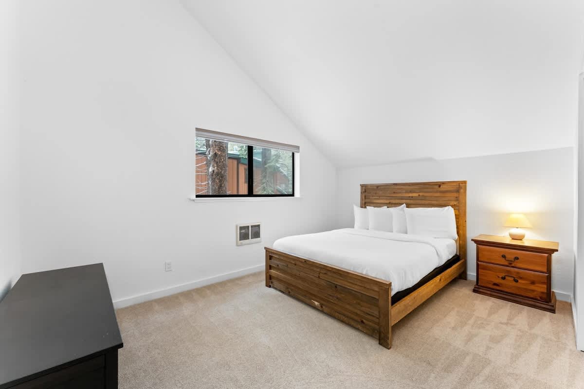 Bedroom with wooden bed and nightstand in a Truckee vacation rental, featuring a slanted ceiling and small window.